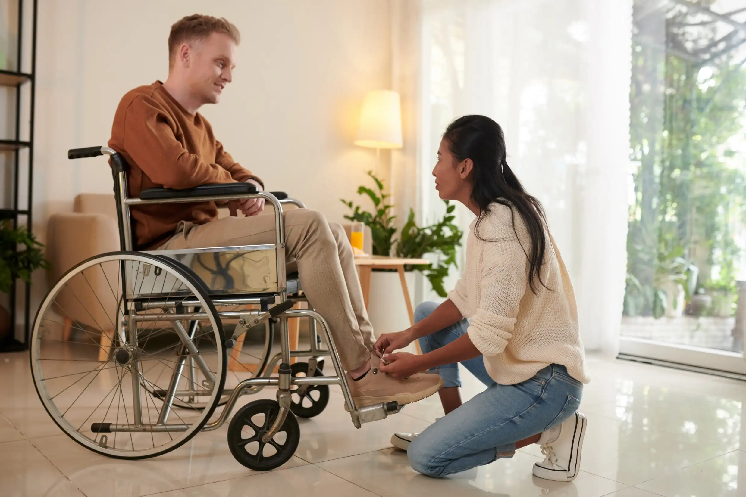 Disabled man in wheelchair having shoes tied by support worker