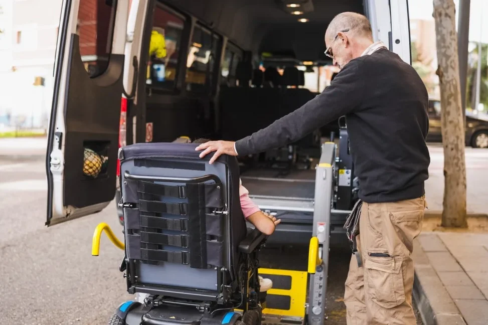 Disabled man in wheelchair getting into van with support workers help